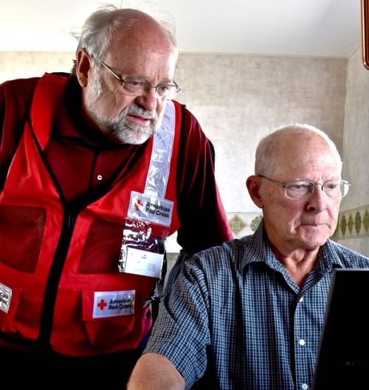 American Red Cross volunteer Bob Wallace looks over the shoulder of Kitchen Site Manager Dan Cenis to view images of the remains of Cenis’ remote cabin that was destroyed by wildfire. Photo Credit: Lloyd Ziel/American Red Cross 